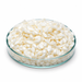 Ivory-white Emulsiphos F wax pastilles in a clear glass laboratory dish on white