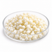 Ivory-white Symbiomuls GC MB emulsifier granules in a clear glass Petri dish on white